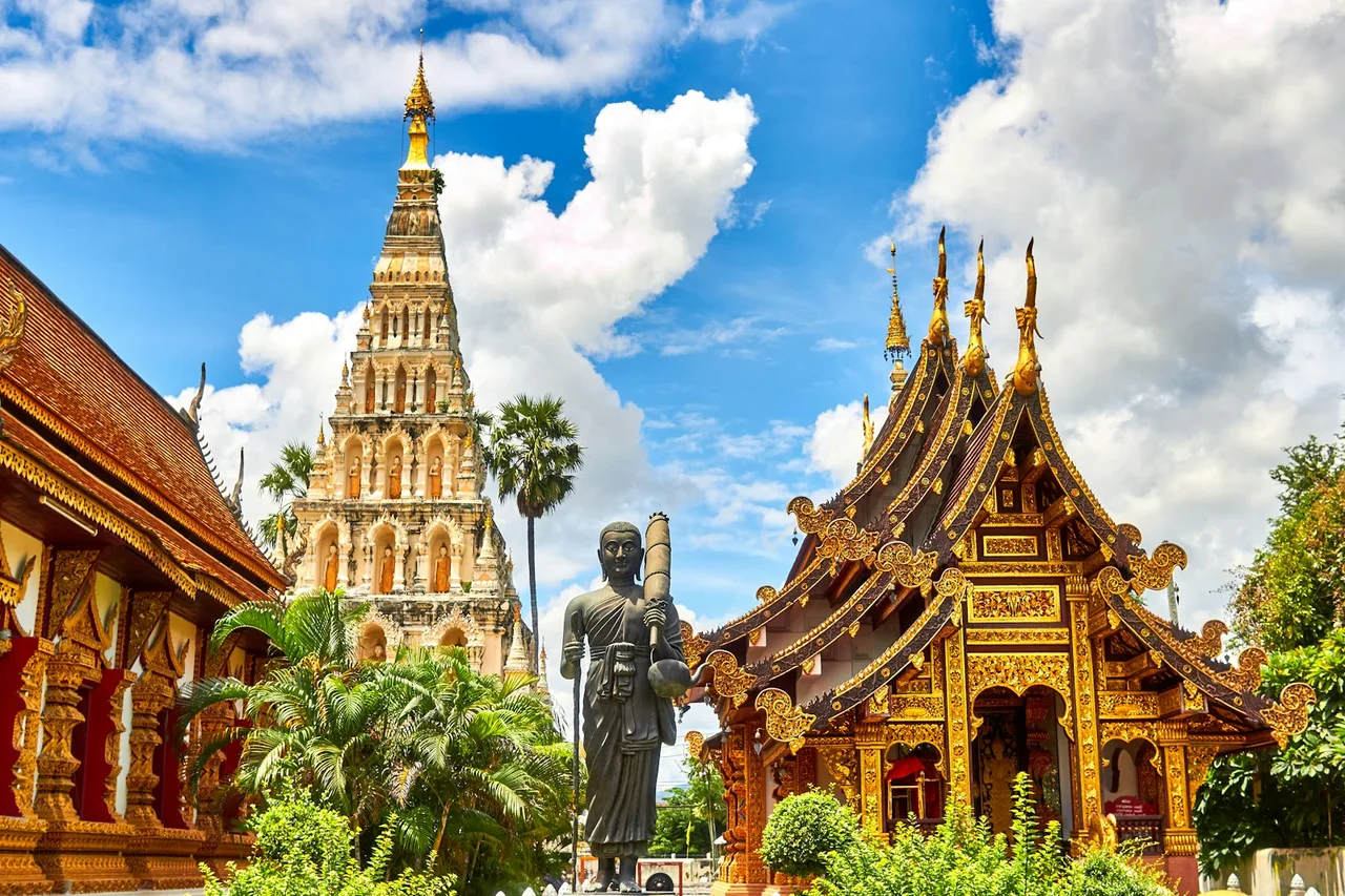 Ornate Thai temple buildings and a statue beneath a blue sky